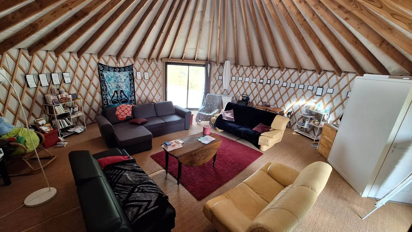 Intérieur de la yourte : charpente en bois, canapés, tapis rouge et lumière naturelle